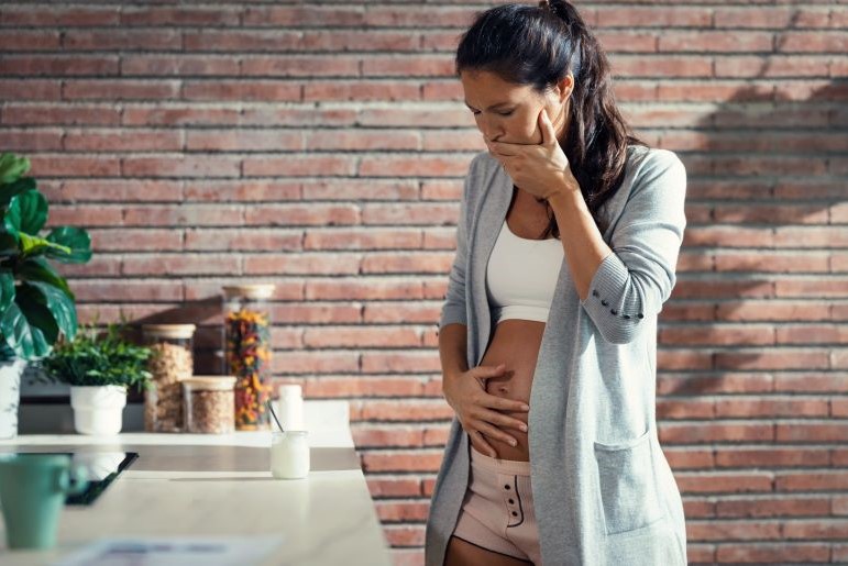 Schwangere Frau in der Küche, Hand auf Bauch und Mund als Ausdruck von Übelkeit.