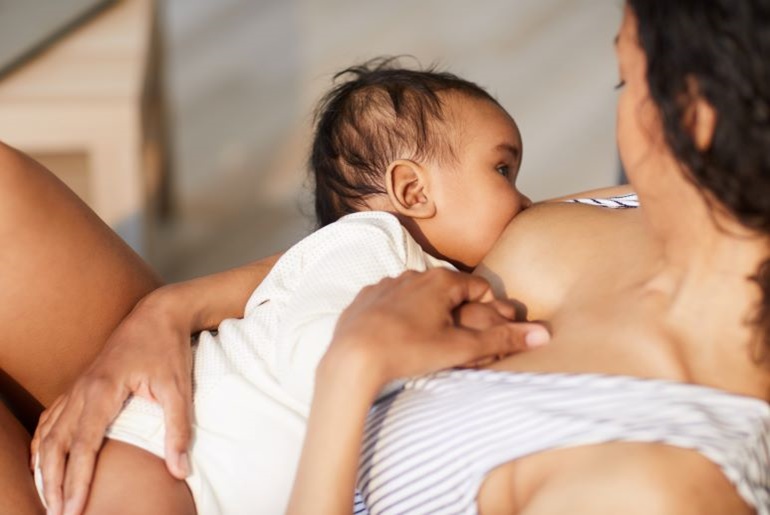 Stillende Mutter hält ihr Baby im Arm, das an ihrer entblößten Brust trinkt. Intimer Moment des Stillens.