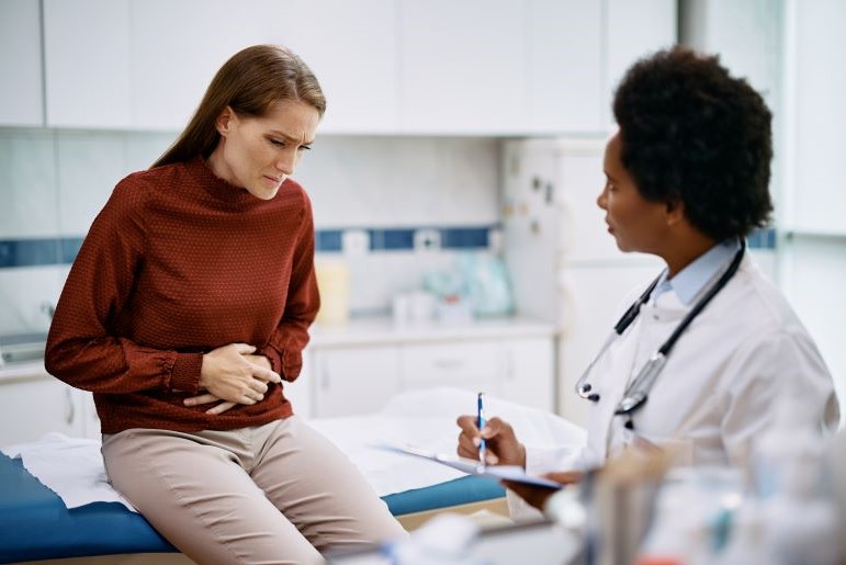 Patientin mit Bauchschmerzen bei Arztbesuch. Ärztin notiert Symptome für Endometriose-Forschung mit KI.