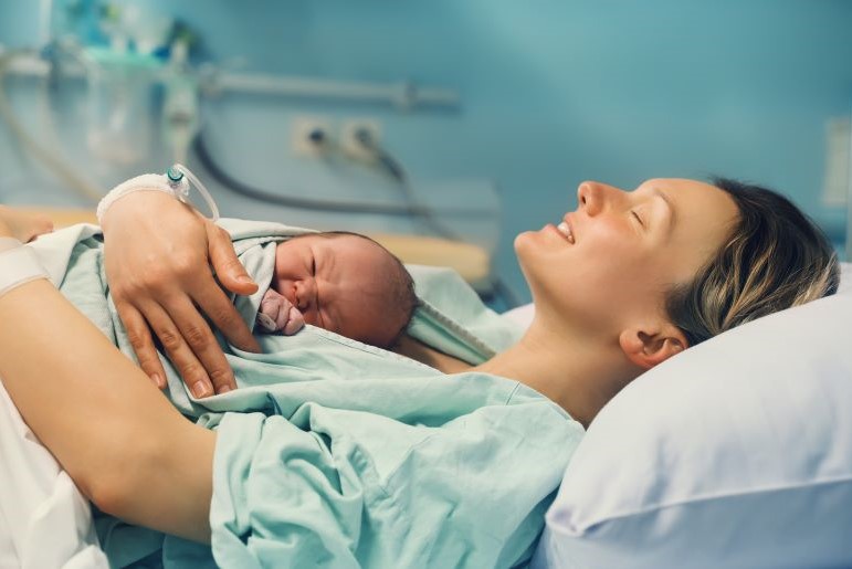 Erschöpfte Mutter hält ihr Neugeborenes nach der Geburt zärtlich auf der Brust im Krankenhaus.