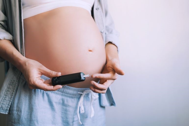 Schwangere Frau kontrolliert Blutzucker am Finger mit Glukosemessgerät zur Überwachung von Gestationsdiabetes.