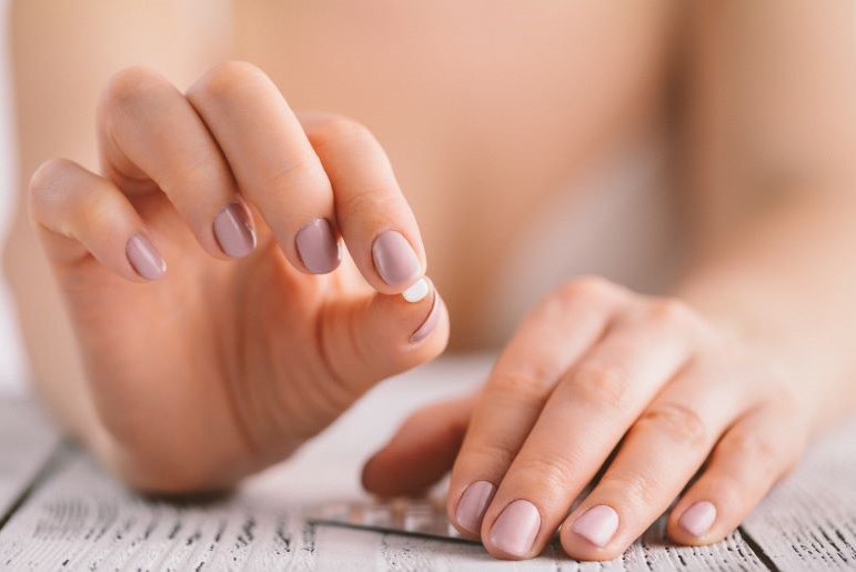 Frauenhand hält kleine weiße Pille für orale Kontrazeption über Blisterpackung auf Tisch.