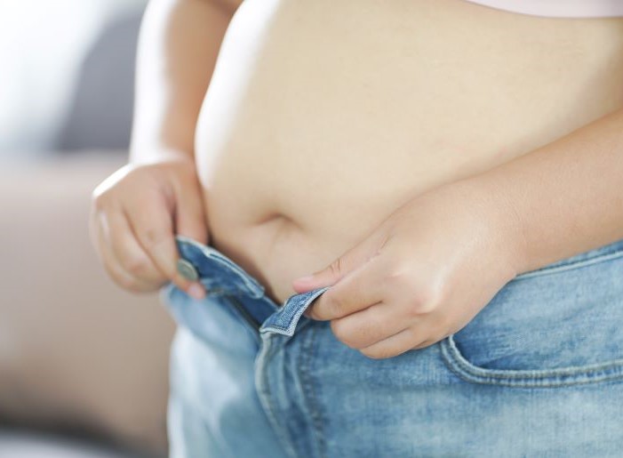 Schwangere Frau mit PCOS-bedingtem Übergewicht versucht, Jeans über ihren Babybauch zu schließen.