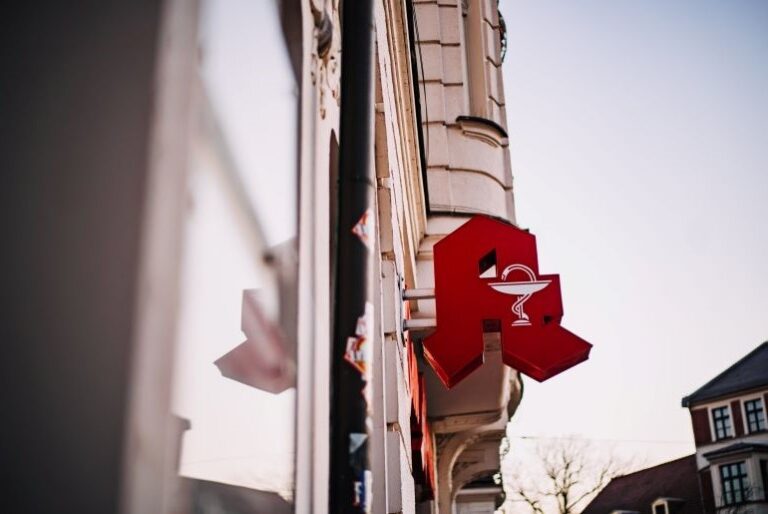 Rotes Apotheken-Schild an einer Hausfassade bei Tageslicht.