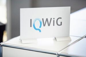 IQWiG Schild auf Tresen mit Logo in Blau und Grau.
