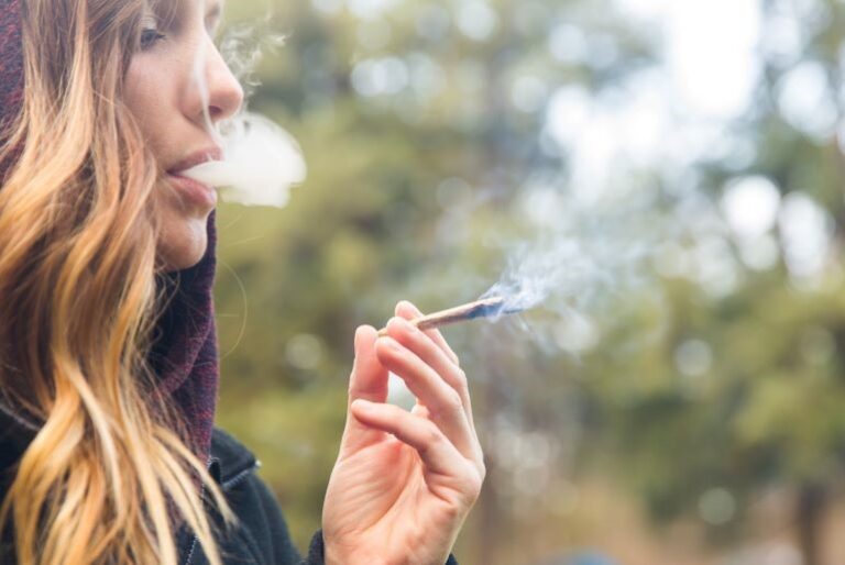 Frau raucht Joint im Freien; Rauchwolke sichtbar. Bezug zu THC, Auswirkungen auf weibliche Fruchtbarkeit.