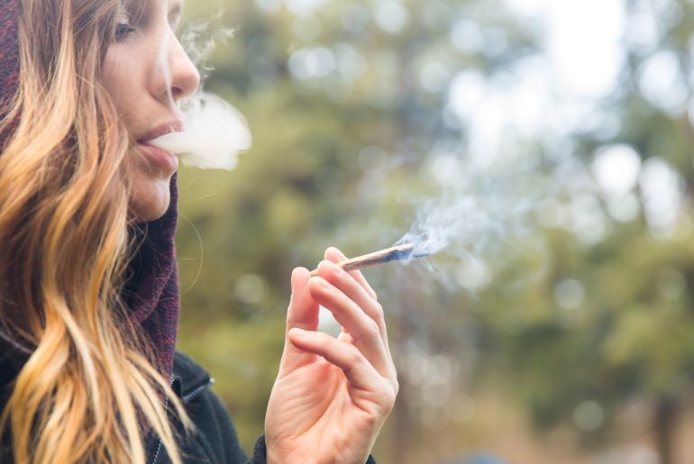 Frau raucht Joint im Freien; Rauchwolke sichtbar. Bezug zu THC, Auswirkungen auf weibliche Fruchtbarkeit.
