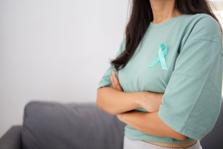 Frau mit tealfarbenem Ribbon auf dem T-Shirt, Symbol für Brustkrebsaufklärung.