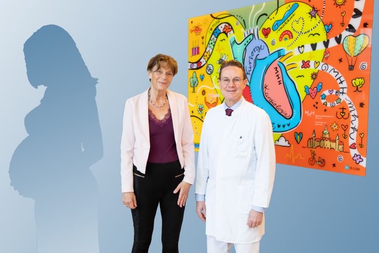 Patientin mit peripartaler Kardiomyopathie steht neben einem Arzt vor einem farbenfrohen Gemälde.