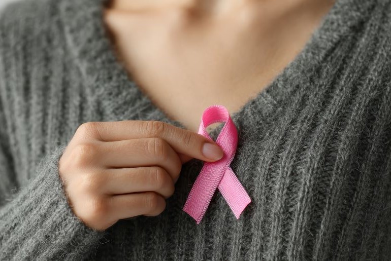 Hand hält eine rosa Schleife, Symbol für Brustkrebsbewusstsein und Unterstützung.