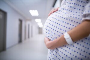 Schwangere Frau in einem Krankenhausflur, die ihren Babybauch hält.