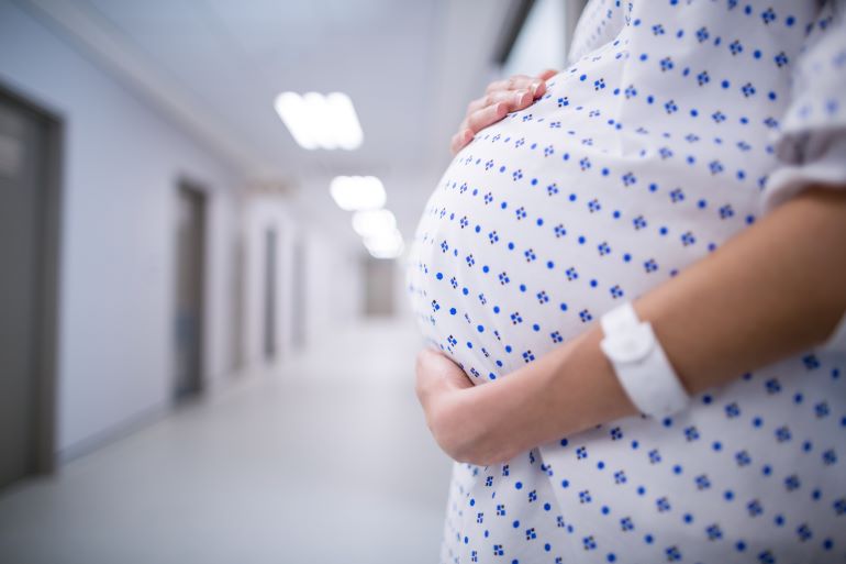 Schwangere Frau in einem Krankenhausflur, die ihren Babybauch hält.