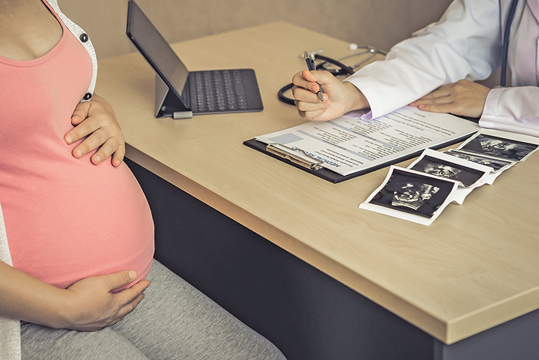 Schwangere Frau bei einer medizinischen Beratung mit Ultraschallbildern und Dokumenten auf dem Tisch.